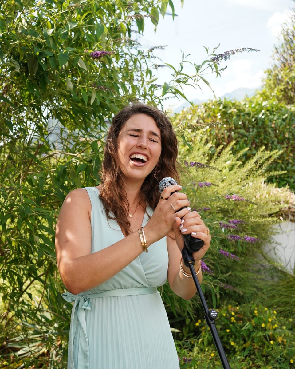 Celya singt mit geschlossenen Augen ins Mikrofon, umgeben von Sommergrün